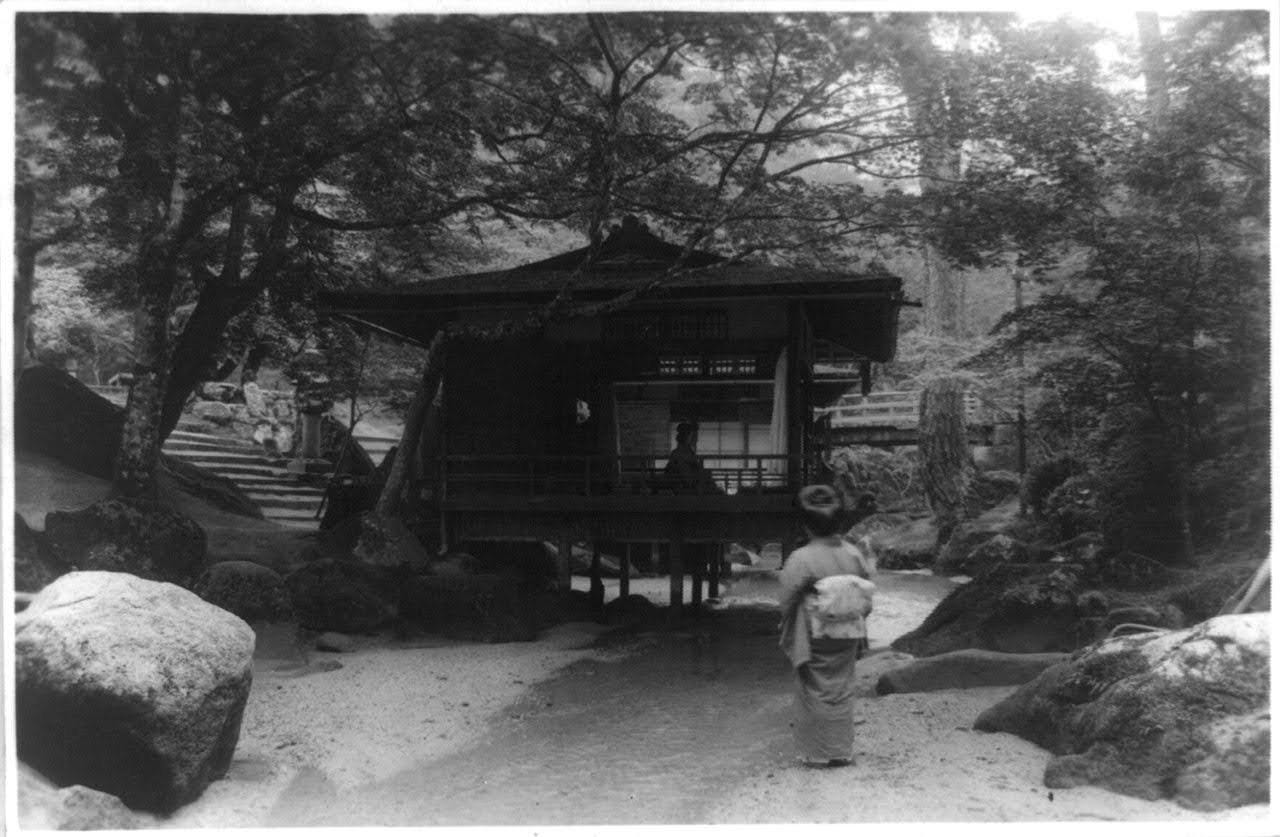 Japanese woman walking through the garden setting of a tea house (Chashitsu) - in the Hiroshima Prefecture, Japan - at the beginning of the 20th century (c. 1900). Japanese woman walking through the garden setting of a tea house (Chashitsu) - in the Hiroshima Prefecture, Japan - at the beginning of the 20th century (c. 1900).