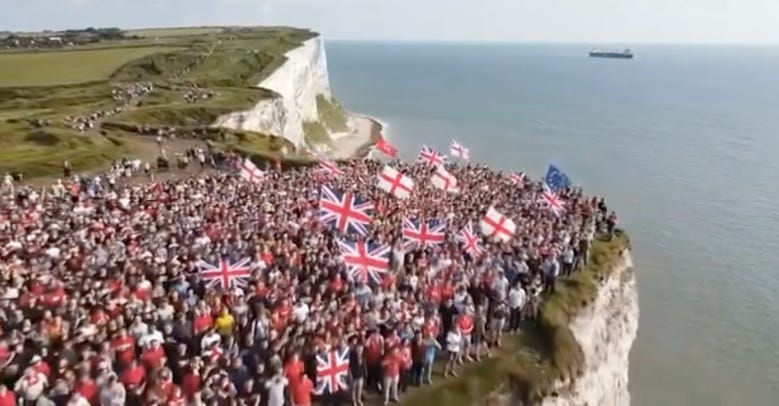 A frame of an 'AI slop' video showing a crowd of British people holding British and English flags at the top of the White Cliffs of Dover.