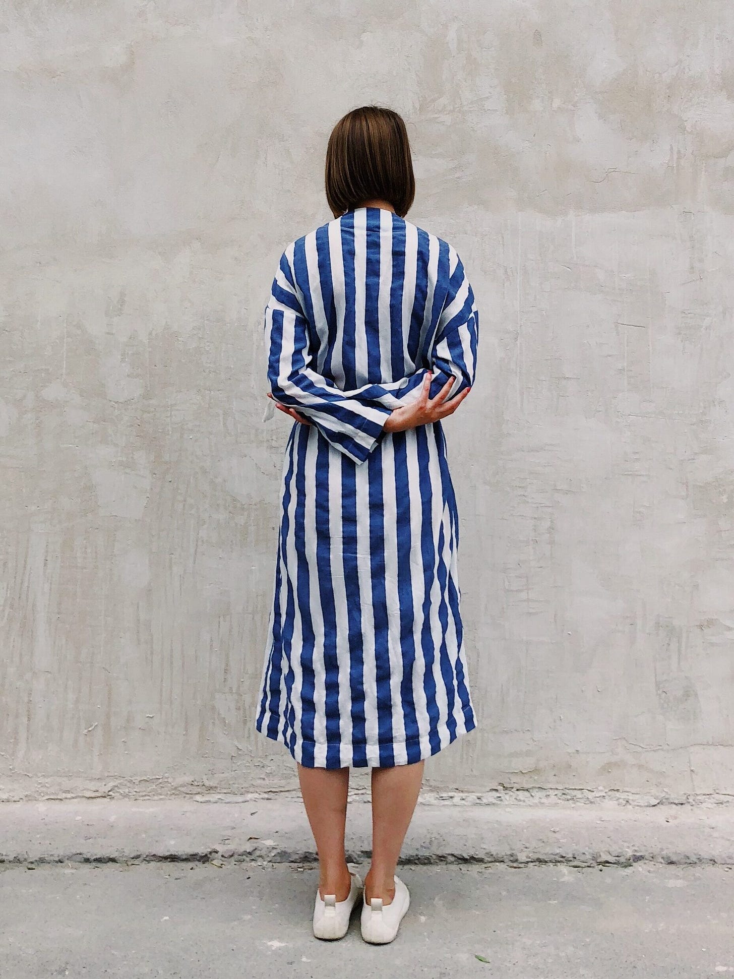 Hitting The Wall (woman in blue and white striped dress, facing away from camera towards stone/plaster wall)