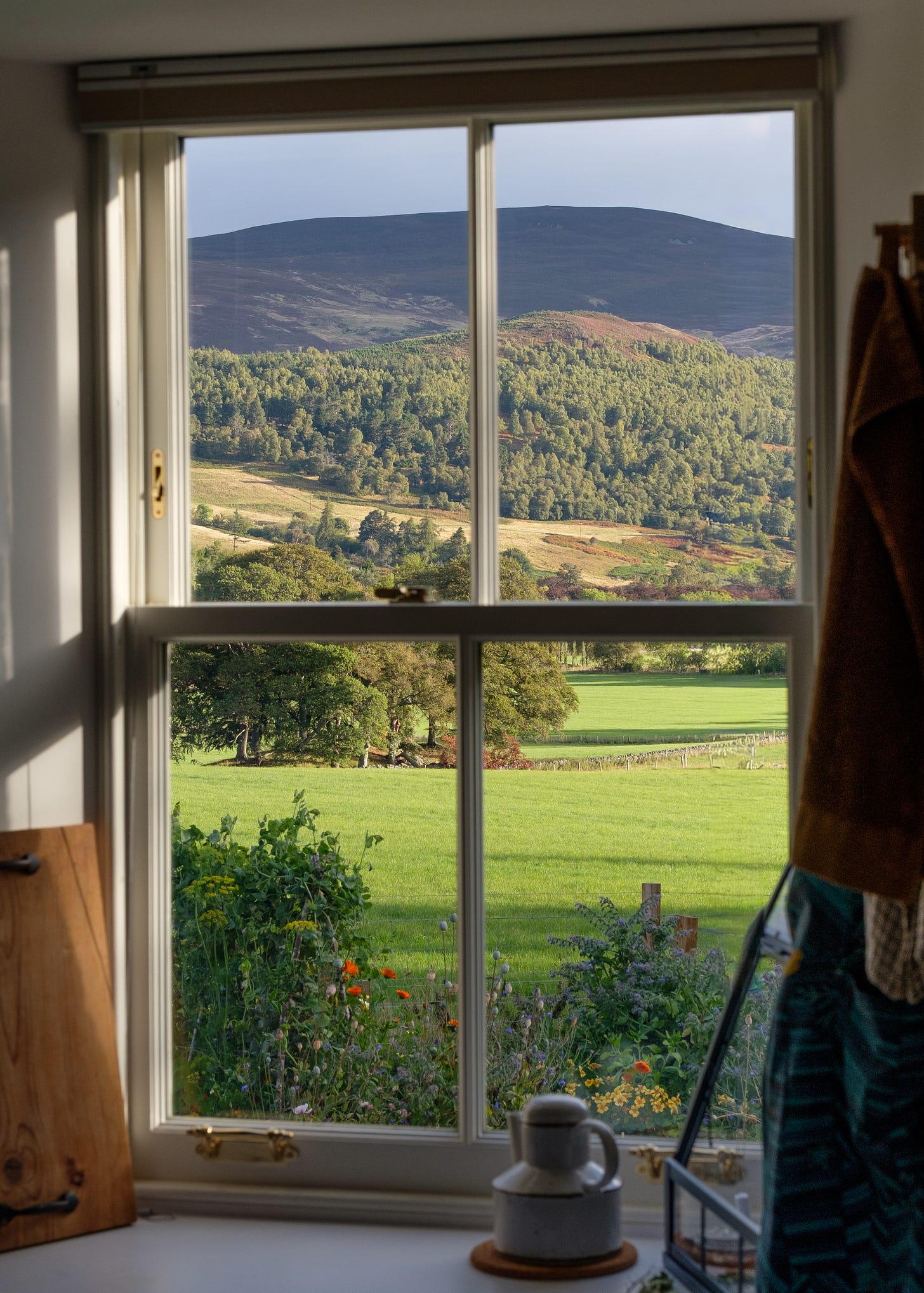 A photo taken from behind an old sash window in a cottage overlooking empty fields and rolling hills. The sunrise lights the scene from the east, bringing a feeling of warmth acorss the land as it comes to life.