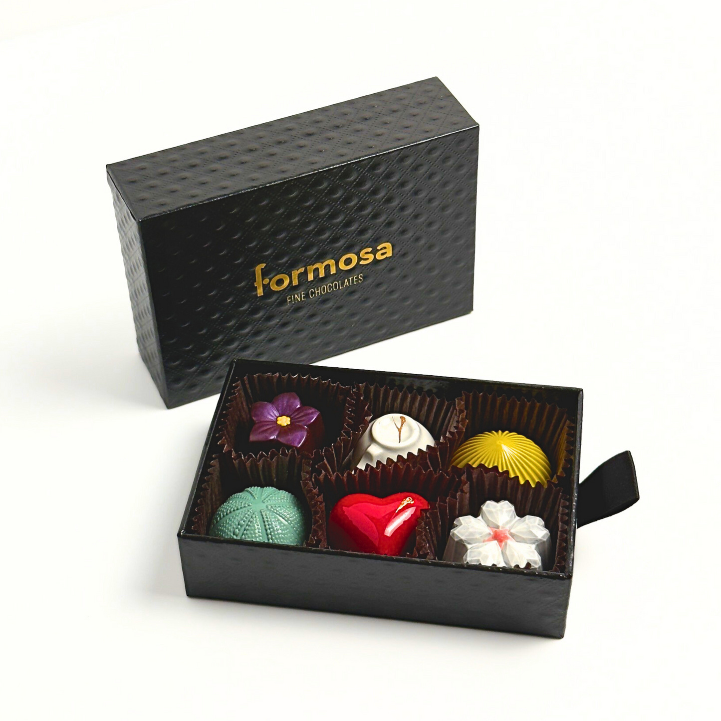 A luxury Formosa brand chocolate box with various colored bonbons neatly arranged in a compartmentalized slot, with the brand name 'Formosa' visible on the exterior in gold color. A luxury Formosa brand chocolate box with various colored bonbons neatly arranged in a compartmentalized slot, with the brand name 'Formosa' visible on the exterior in gold color.