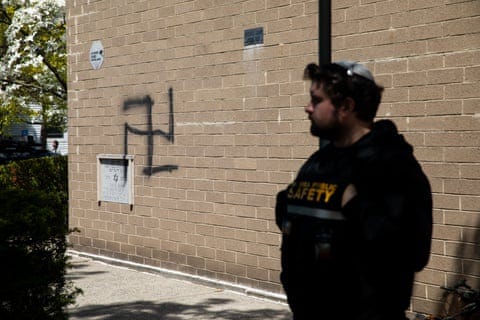 a man stands outside a synagogue where a spray-painted swastika is visible