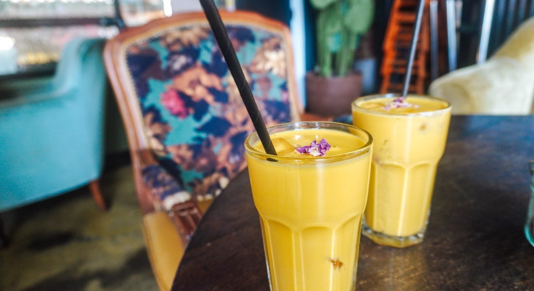 A pair of mango lassis on a wooden table with a chair opposite them