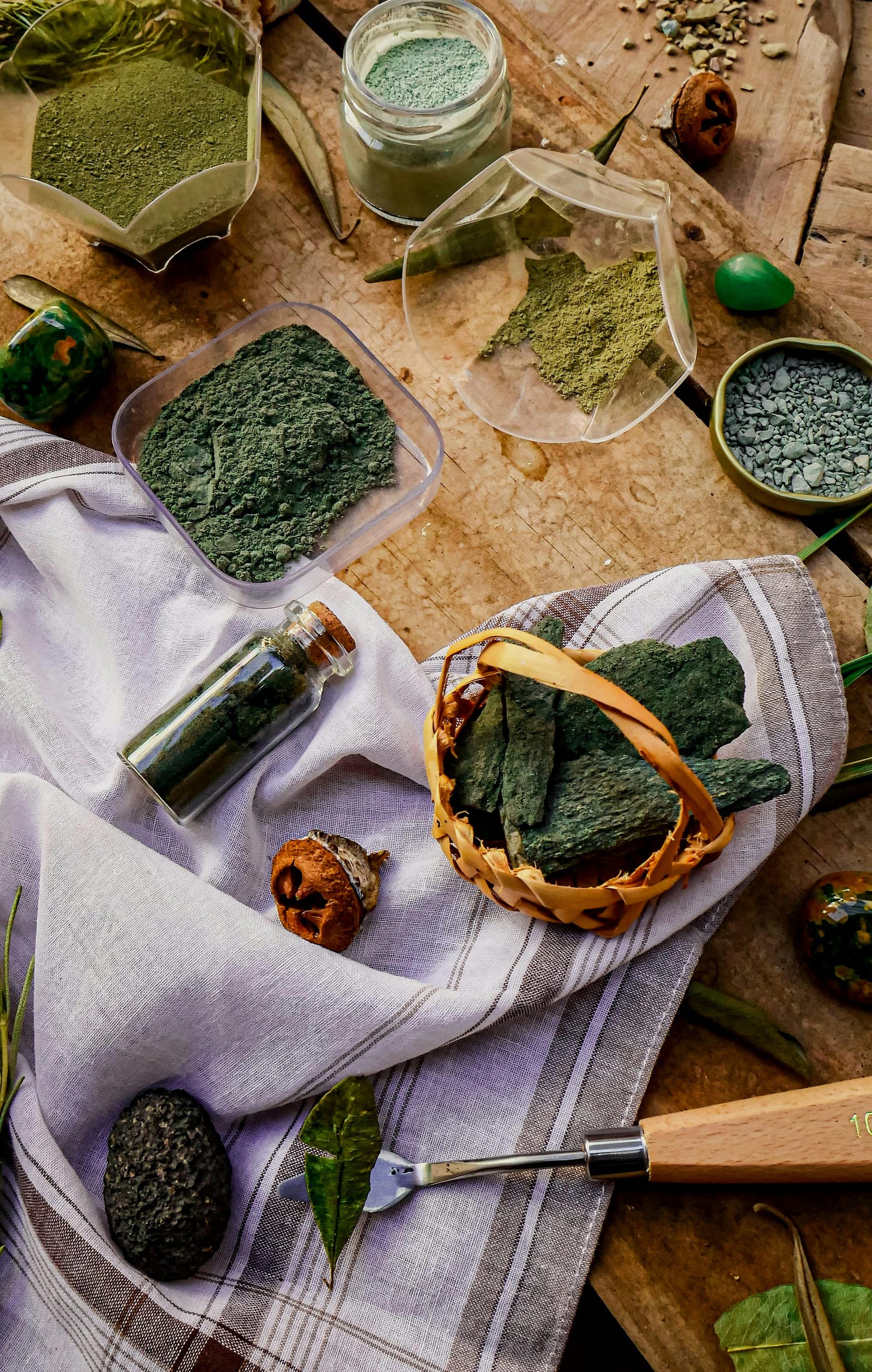 Natural green pigments for paint in various containers, with shells and rocks, on a wooden table