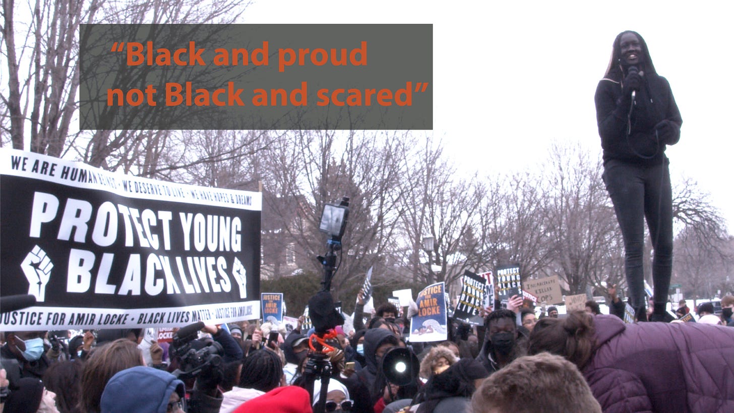 young Black girl stands above crowd next to a sign reading "protect young black lives" young Black girl stands above crowd next to a sign reading "protect young black lives"