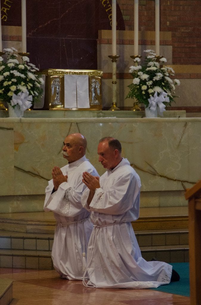 Ed Schaub, left, and John Cormack, right, kneel during their ordination.