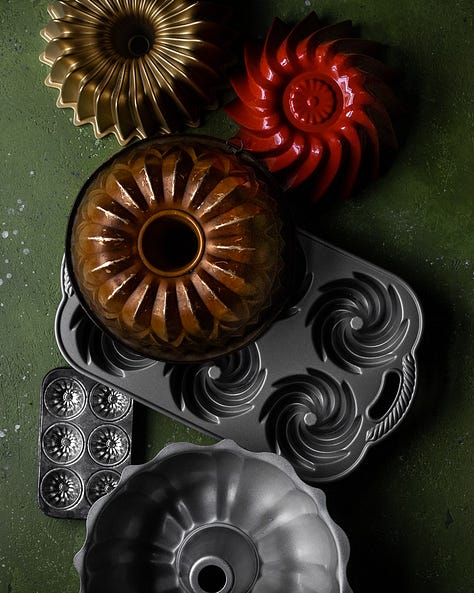 An overhead shot of vintage Bundt pants on a green background. A photo of orange carrots on a green background. A photo of shredded carrots in the foreground and the rest of the ingredients for Carrot and cranberry gingerbread cake. An overhead shot of the finished bundt cake with cream cheese frosting and sugared cranberries on top with white twinkle lights in the foreground and background. Another photo of the finished carrot and cranberry gingerbread cake surrounded by pine garland and white twinkle lights. 