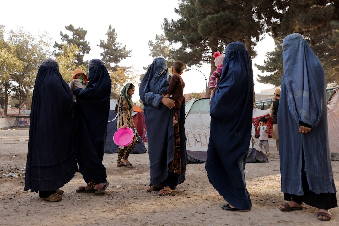 Displaced Afghan women in burqas hold children in a temporary camp, highlighting the human impact of the ongoing humanitarian crisis