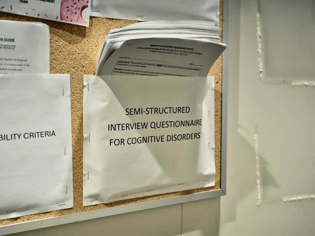 A piece of paper that says "semi-structured interview questionnaire for cognitive disorders" is stapled to a bulletin board and holds questionnaire packets.