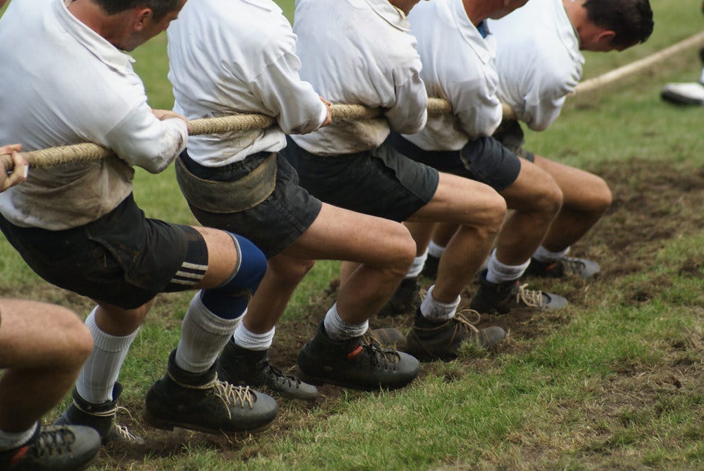Color photograph of multiple people in tug-of-war in a muddy field Color photograph of multiple people in tug-of-war in a muddy field