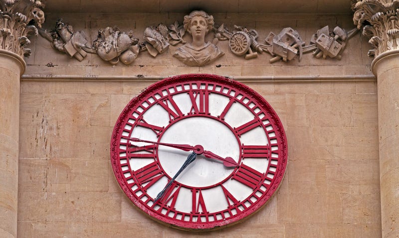 A red and white clock against a stone building wall