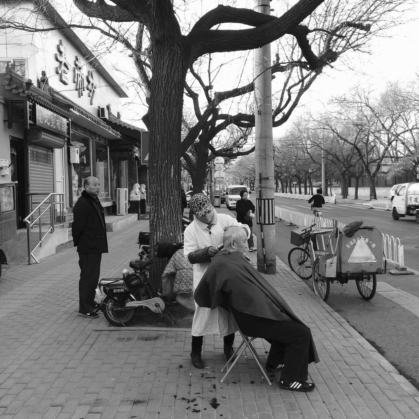 Man getting a haircut on the street in Beijing.