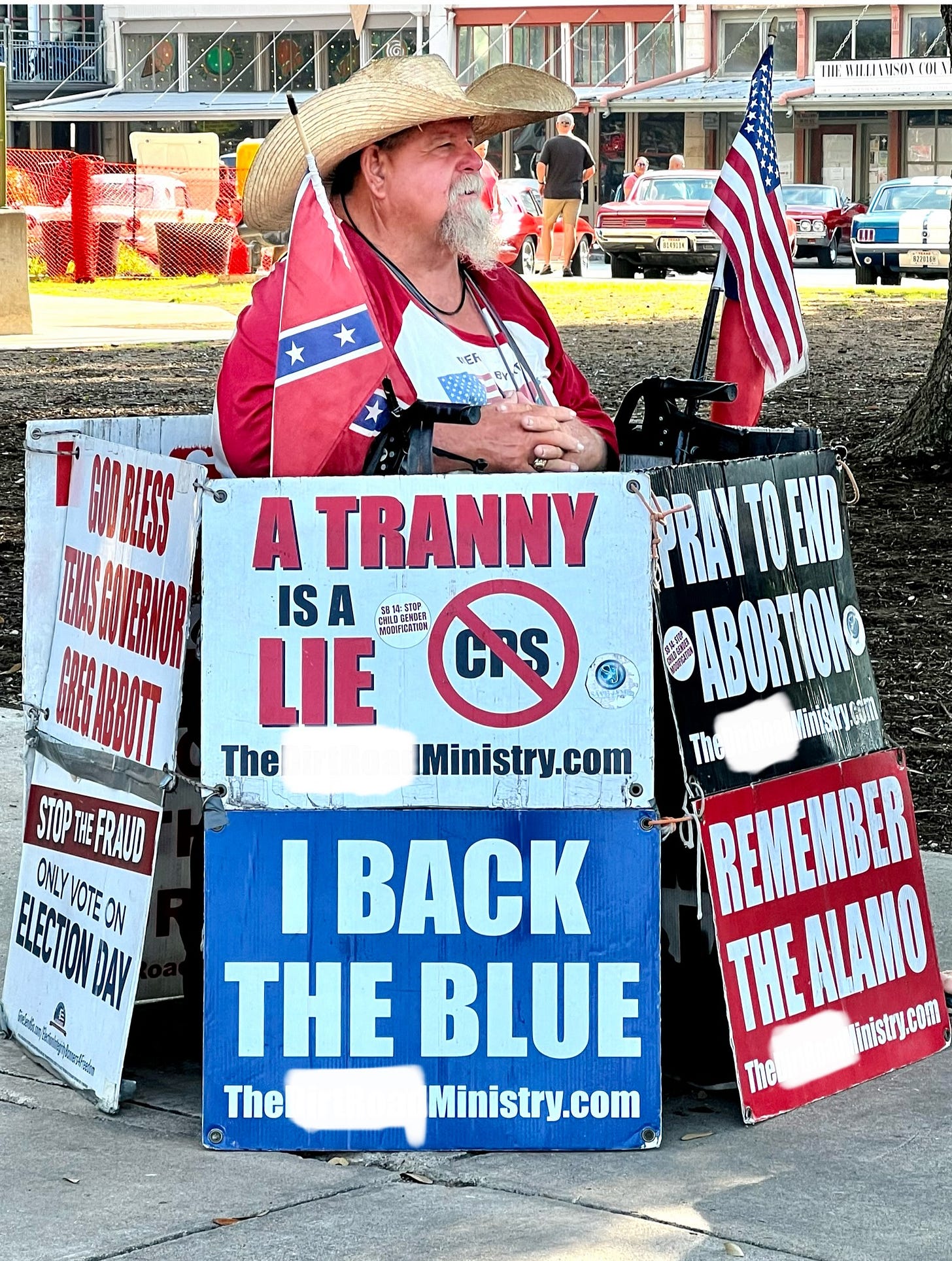 A Christian Nationalist in a small town, Texas Square, with multiple signs that are hate-filled, preaching to the children, grooming them into Christian Nationalism. A Christian Nationalist in a small town, Texas Square, with multiple signs that are hate-filled, preaching to the children, grooming them into Christian Nationalism.