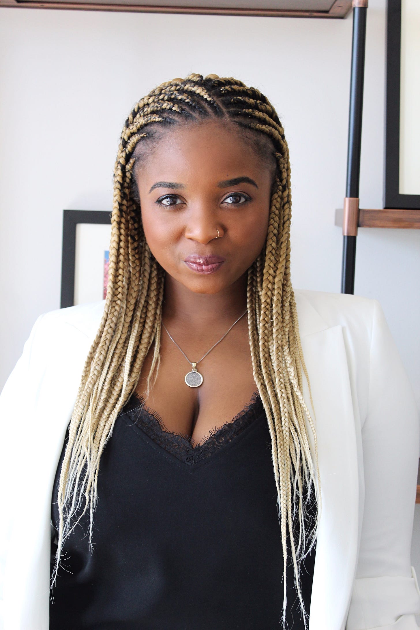 Portrait of Tiffany Chanel Knighten. She is standing in front of a white wall, wearing a white blazer and black top.
