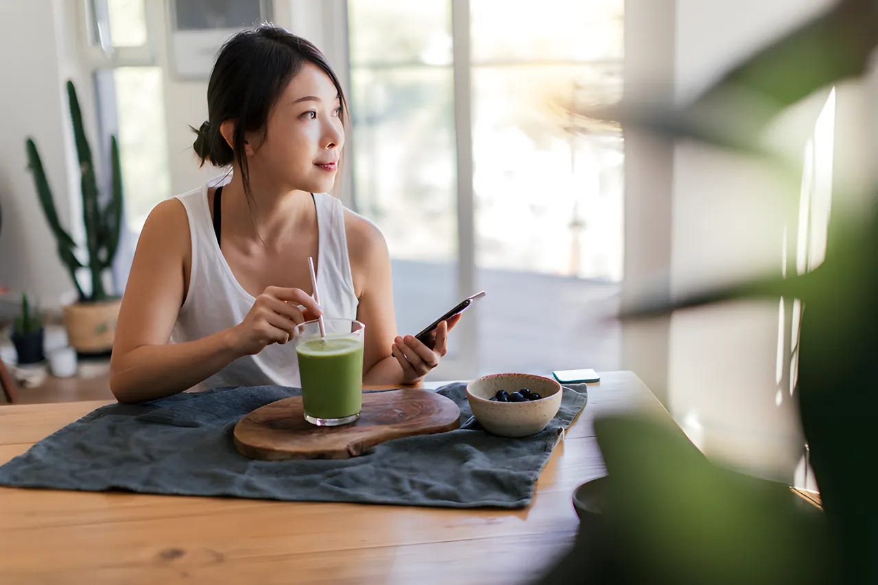 Woman sitting at a table sipping on a matcha latte and looking out the window.