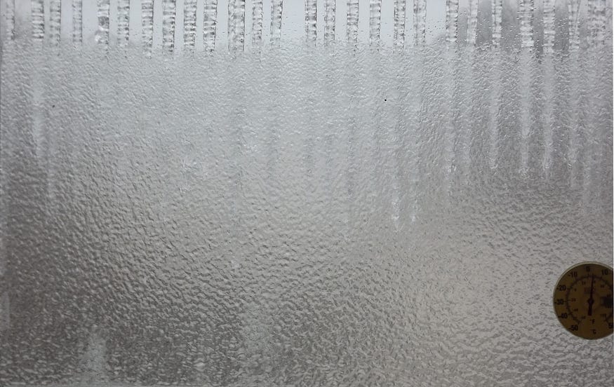 Freezing rain ices a pane of glass, blocking the world from view, except for the faint outlines of massive icicles.