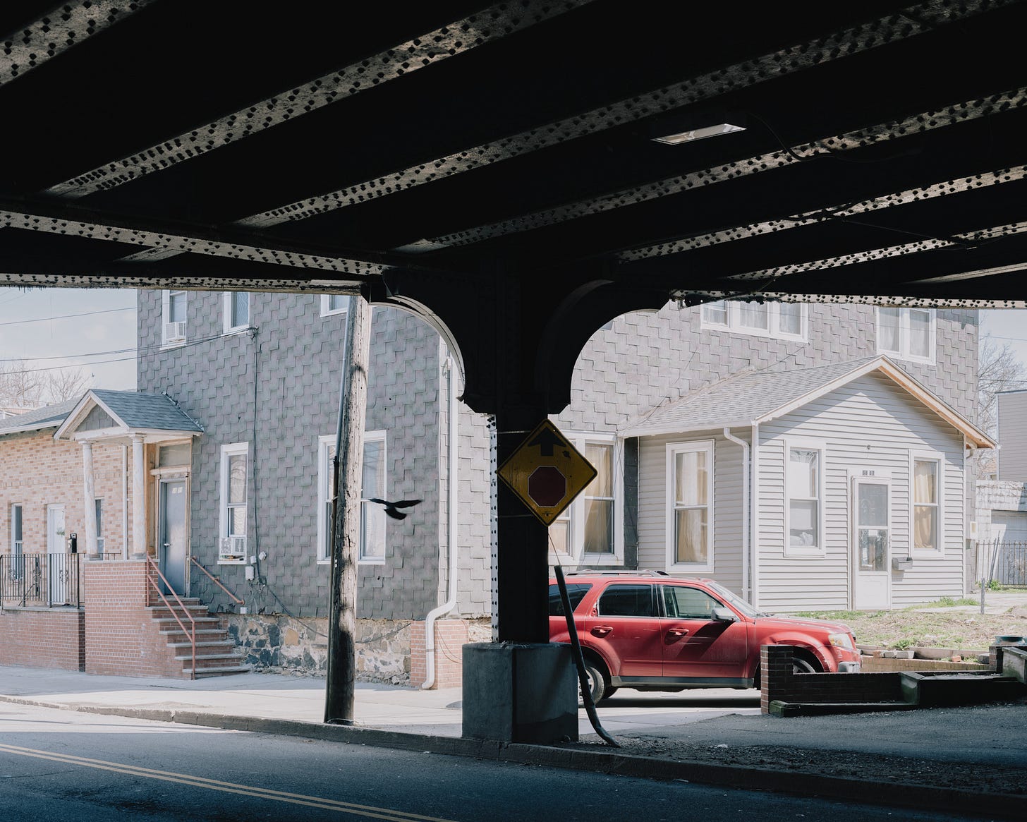 View of house from underneath train tracks with pigeon in flight and red SUV
