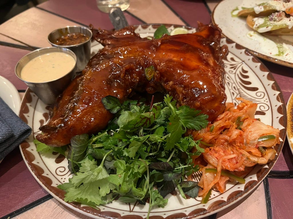A large plate, with a large brown glazed piece of fish collar, with green herbs and kimchi in front, and 2 sauces on the left