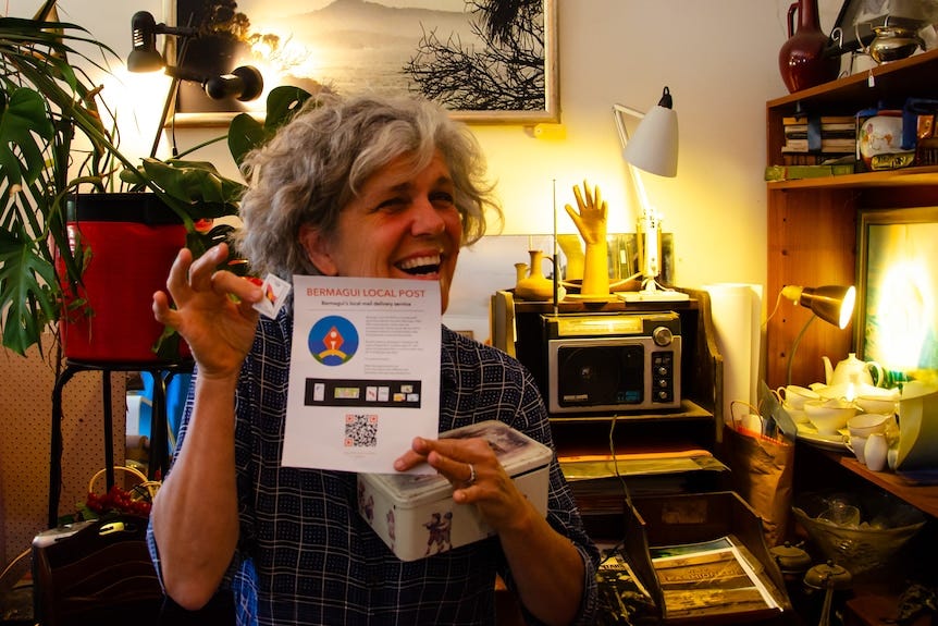 A woman holds up a stamp and a flyer advertising the Bermagui Local Post. A woman holds up a stamp and a flyer advertising the Bermagui Local Post.