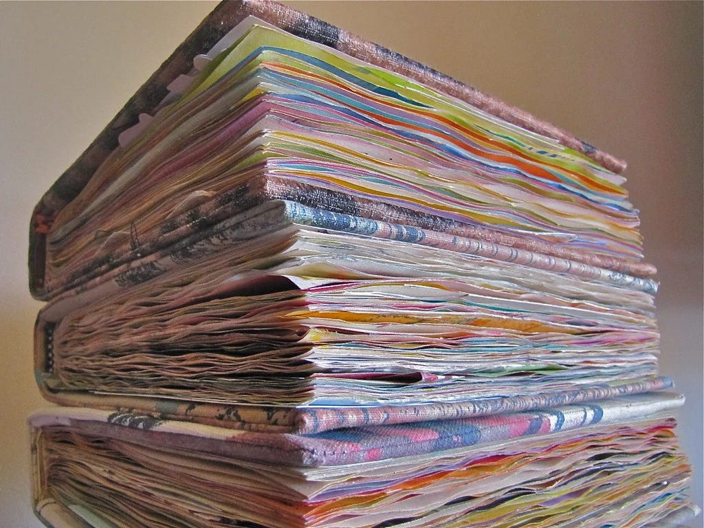 A close-up of well-used journals or notebooks stacked on top of each other, with colorful pages visible from the side.