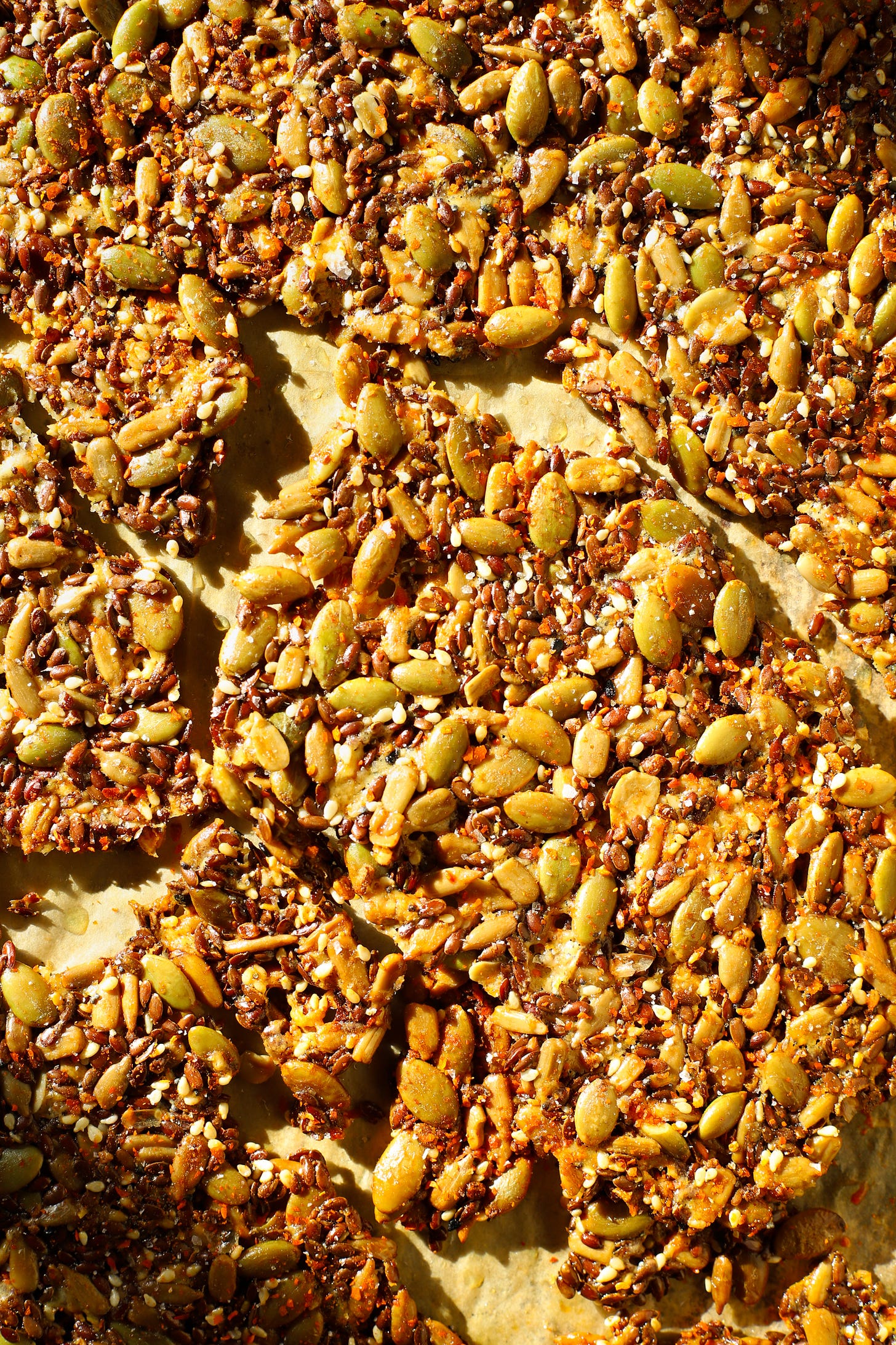 Close-up of gluten-free seeds and cheese crackers on a sheet pan, partially broken