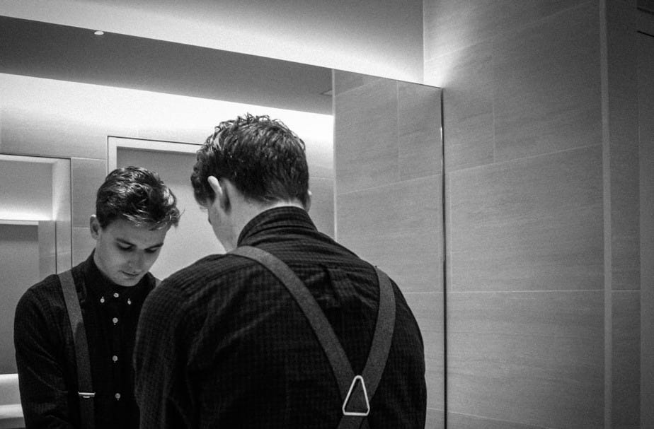 grayscale photography of man standing front of mirror