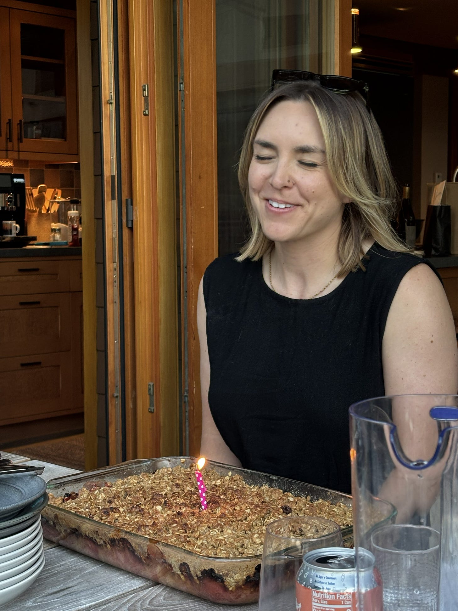 Cassidy closing her eyes to make a wish, with a birthday rhubarb crisp in front of her with a candle in it.