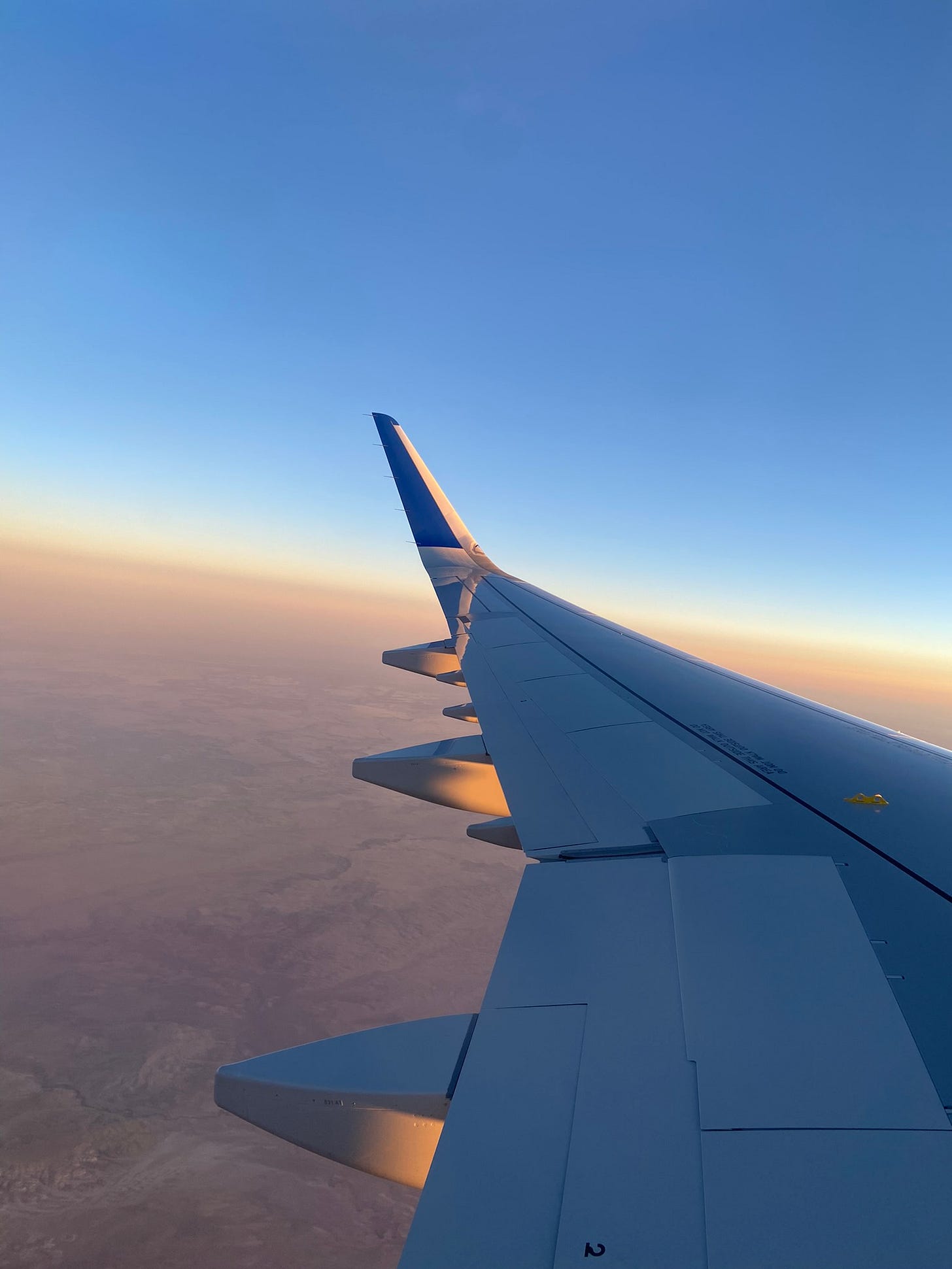A view from a plane window of the the plane wing and a sunset over the desert