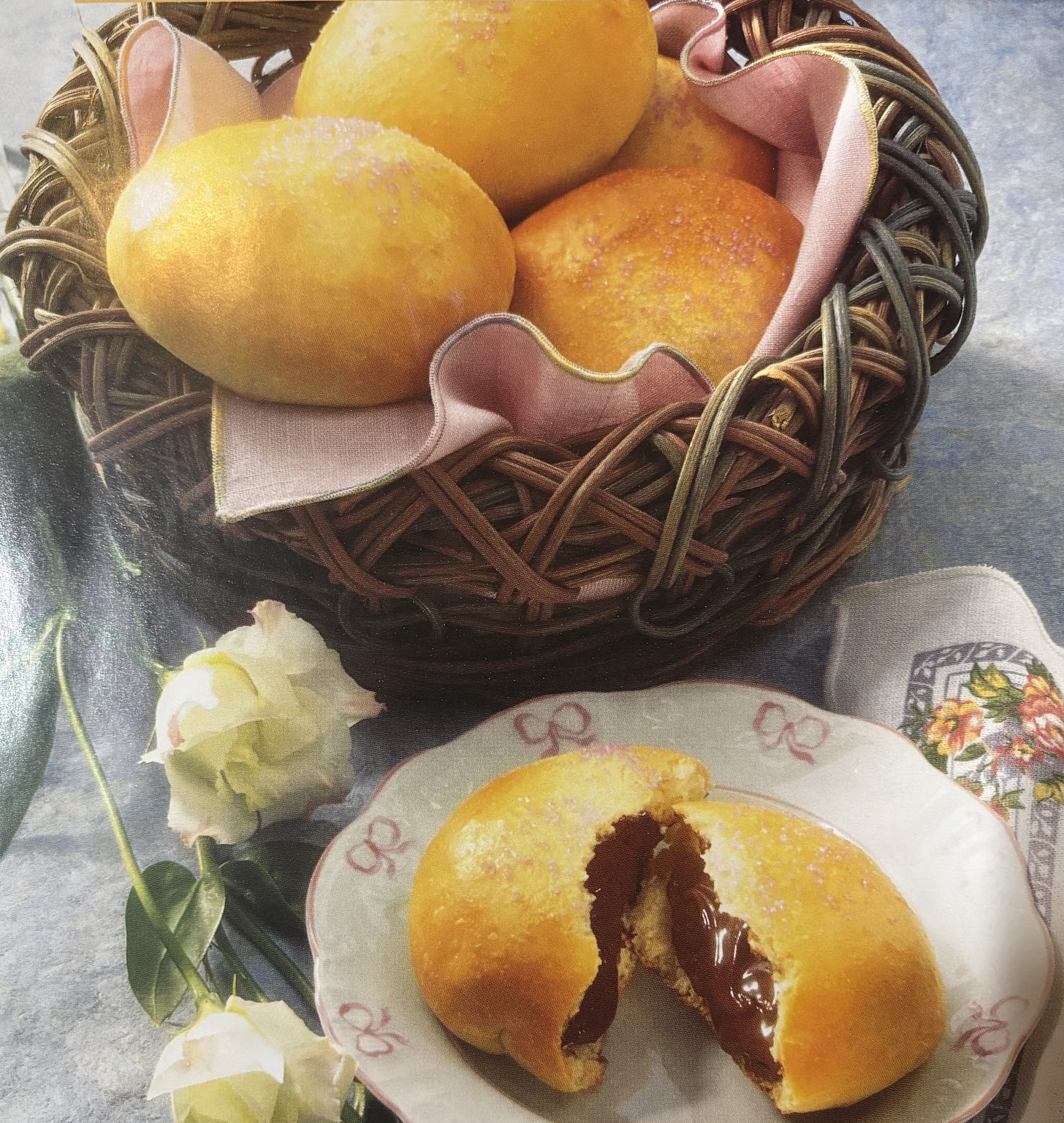 A basket of bread rolls sits next to one on a plate that's broken in half with chocolate oozing out A basket of bread rolls sits next to one on a plate that's broken in half with chocolate oozing out