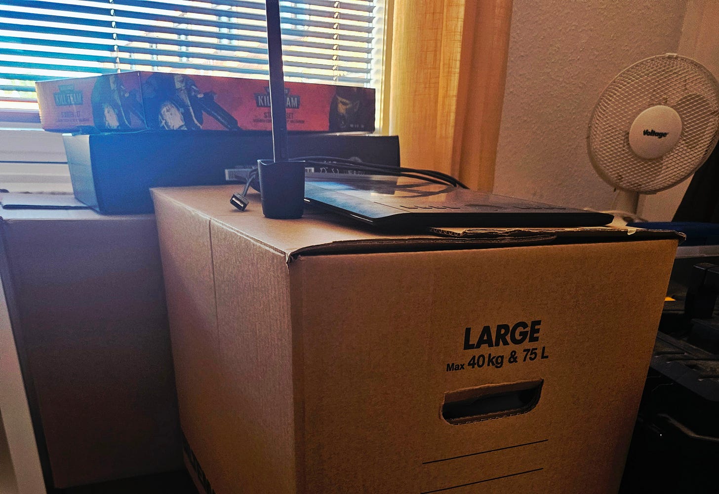 Moving boxes with a bunch of other boxes on top and a fan to the right