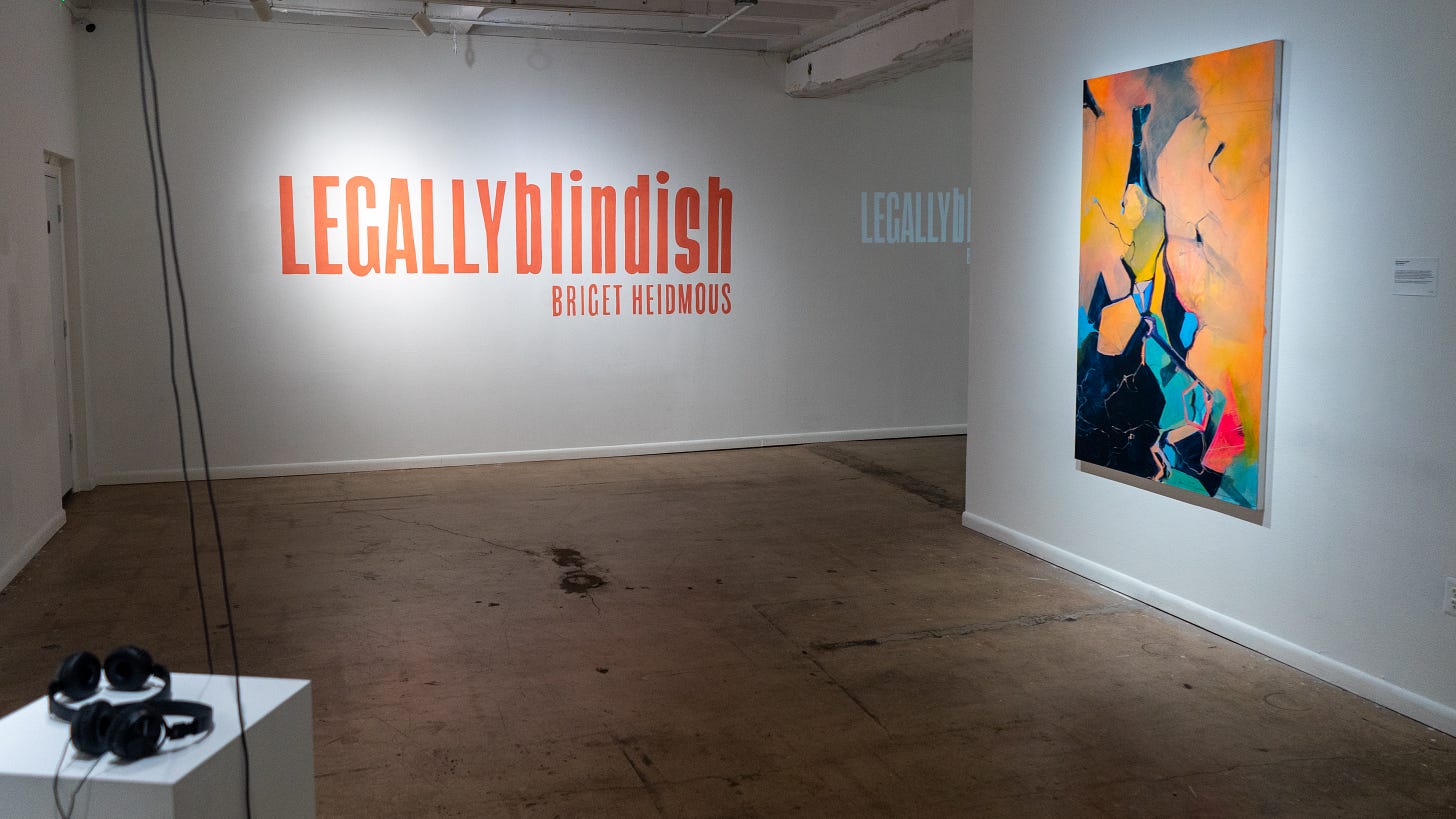 The image is an interior shot of the Culture House Gallery. The floors are cement, and the walls are white. In the bottom left is a podium with two headphones resting on top. At the center-right is a wall with one large abstract painting. On the back wall is the title of the show “Legally Blindish” and the artist’s name, Briget Heidmous. The image is an interior shot of the Culture House Gallery. The floors are cement, and the walls are white. In the bottom left is a podium with two headphones resting on top. At the center-right is a wall with one large abstract painting. On the back wall is the title of the show “Legally Blindish” and the artist’s name, Briget Heidmous.