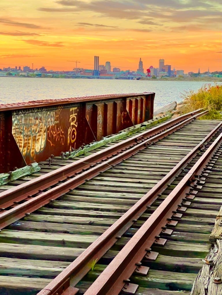 Abandoned railway bridge along the East Bay Bike Path near Kettle Point in Providence, Rhode Island, featuring rusted metal beams and overgrown tracks curving into fog — a forgotten industrial relic set against a backdrop of autumn trees and quiet stillness.