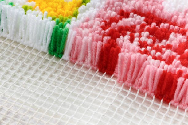 Latch hook rug with yarn in white, gren, pink, red, and yellow on a white canvas