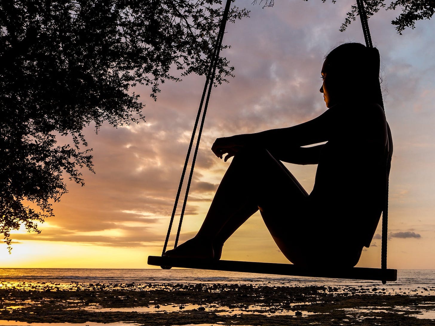 silhouette of woman on swing during golden hour