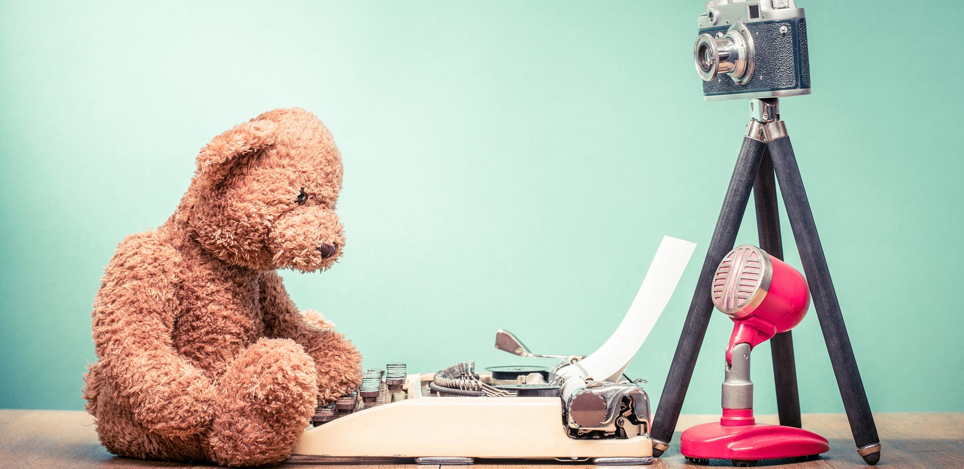 Teddy bear with a typewriter, camera, and microphone representing a writing podcast.