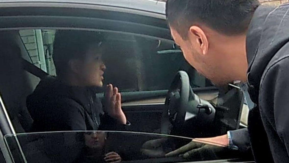 A man talks to another man through a car window.