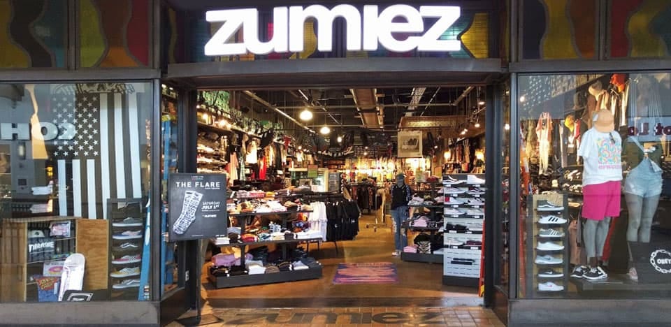a photo of a Zumiez storefront circa perhaps 2014, wherein the eclectic design of the store's aesthetic is strikingly visible. The window display includes a black and white American flag.