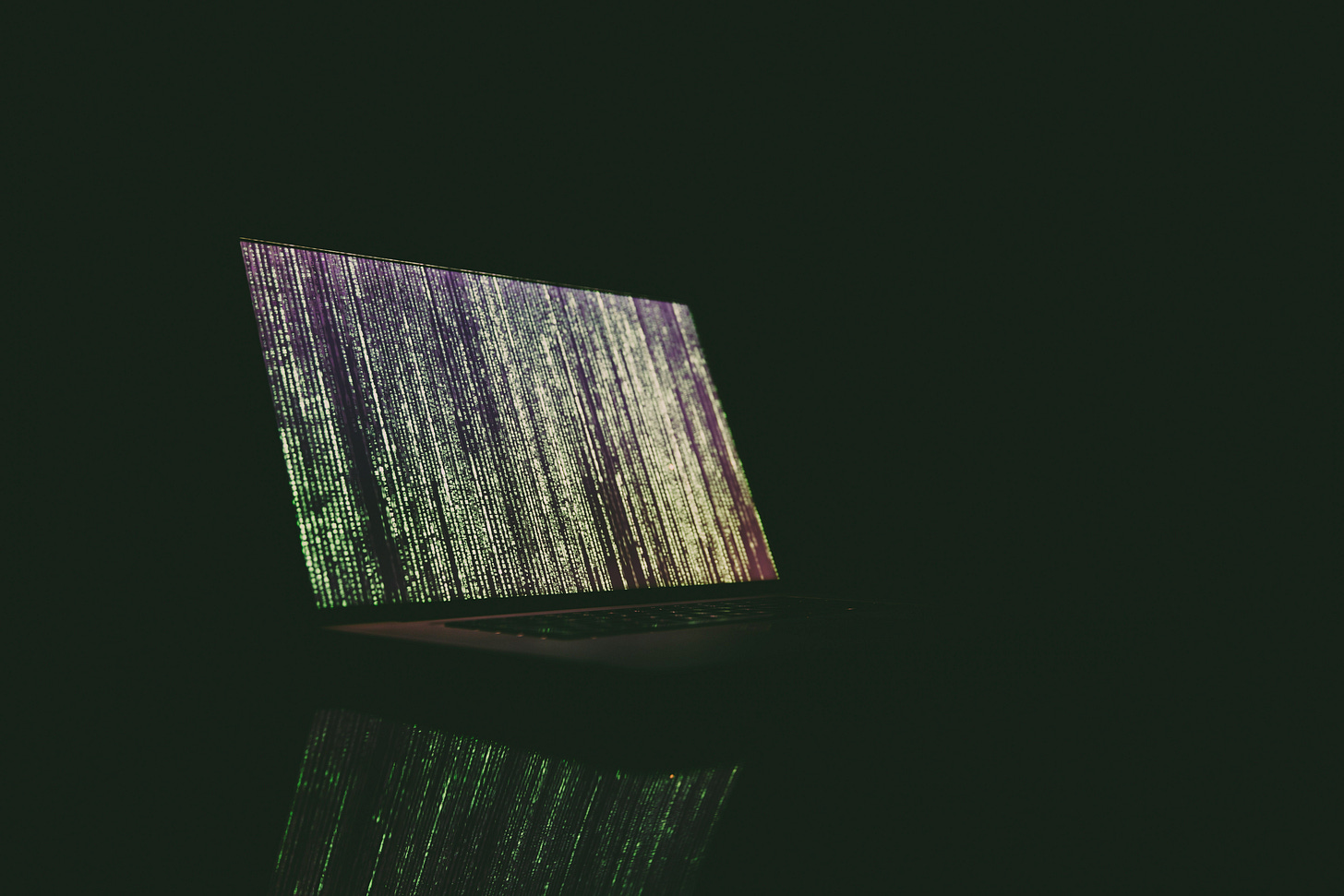 a laptop computer sits on top of a table in the dark. everything is black except for the computer screen - lit up with glowing vertical green lines of runes and characters, the Matrix screen saver from the movie "The Matrix" a laptop computer sits on top of a table in the dark. everything is black except for the computer screen - lit up with glowing vertical green lines of runes and characters, the Matrix screen saver from the movie "The Matrix"