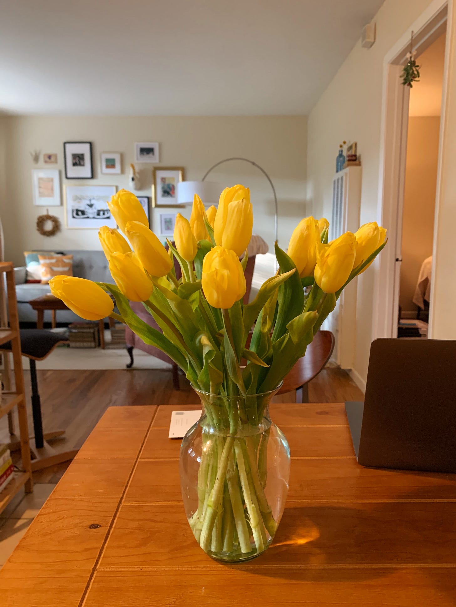 A bright yellow bouquet in a vase sits on a wooden table.