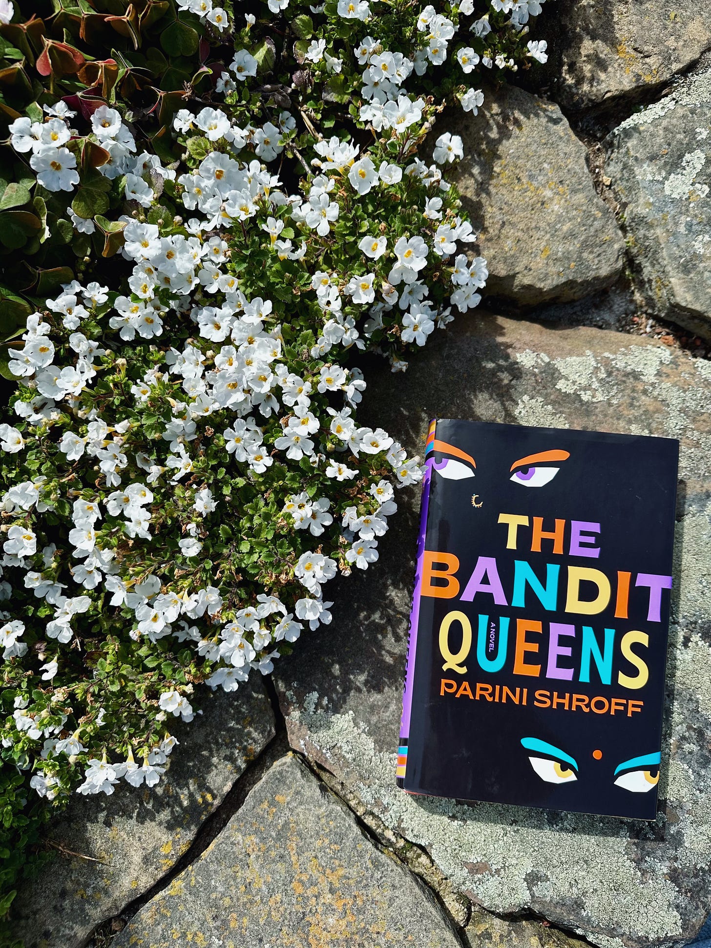 The Bandit Queens on a stone ledge next to white flowers