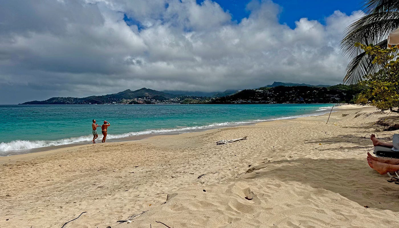 People walking along Grand Anse beach in Grenada with turquoise water and mountains in the distance