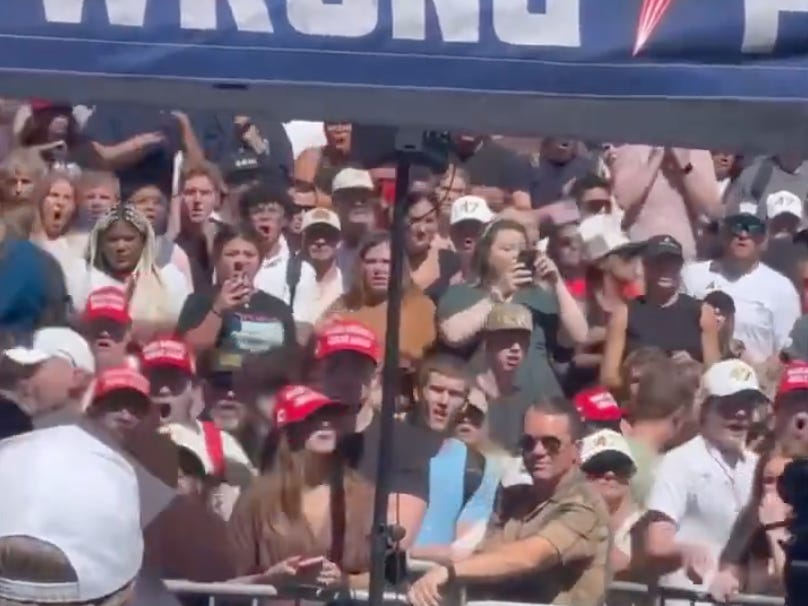 A crowd of students gasping and holding up smartphones as an event unfolds on campus.