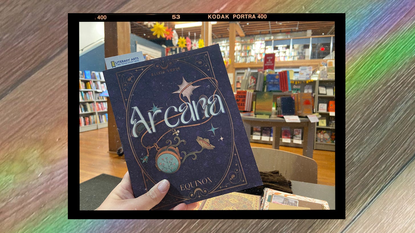 A copy of the Elixir Verse Equinox: Arcana (a book with a mystical purple cover that shows a gold locket) being held up by a white hand in a local Portland bookstore