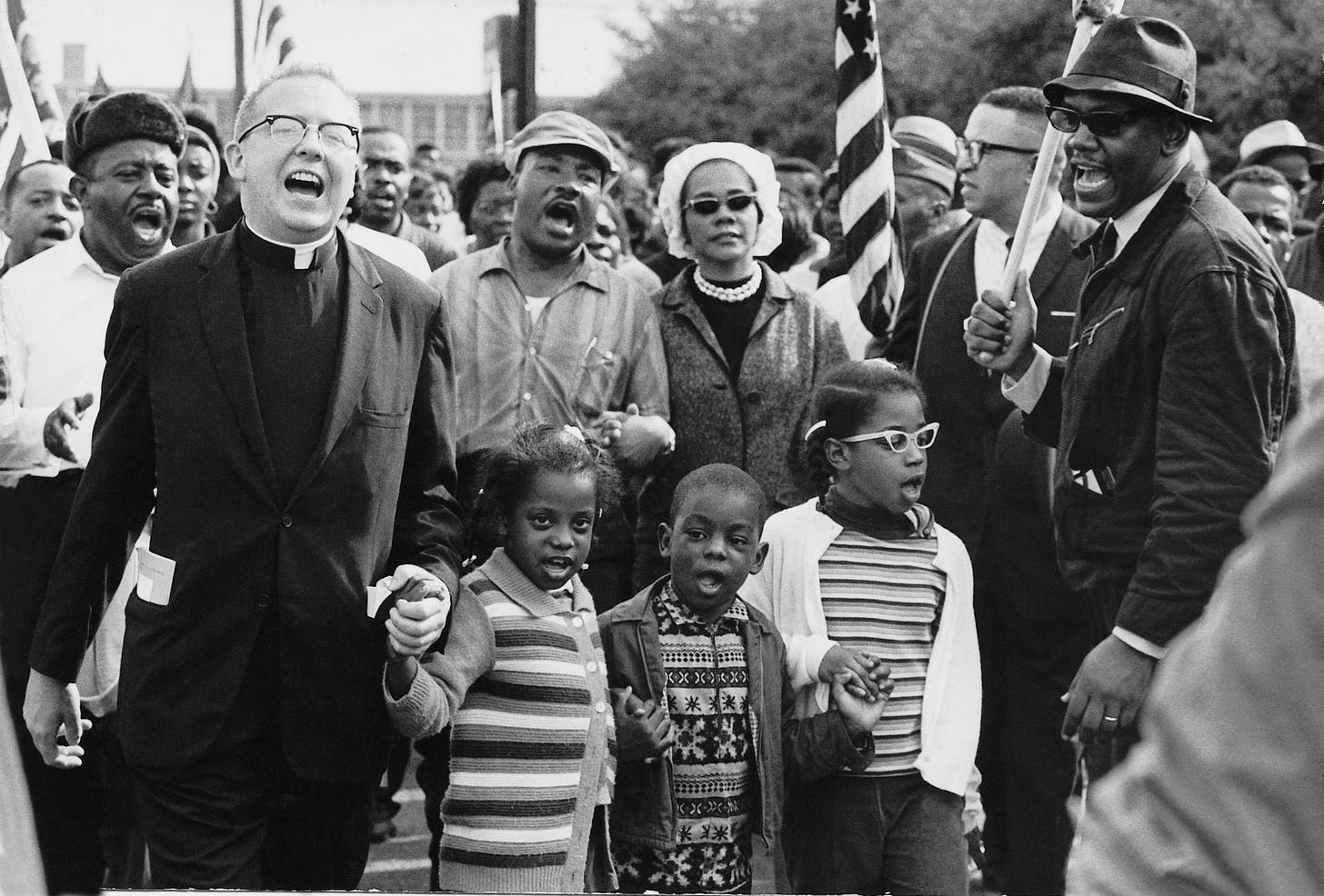 Black and white photo of Rev. Martin Luther King, Jr., his wife Coretta, the Abernathy family, Rev. James Reeb, and many others marching. They appear to be singing. Black and white photo of Rev. Martin Luther King, Jr., his wife Coretta, the Abernathy family, Rev. James Reeb, and many others marching. They appear to be singing.