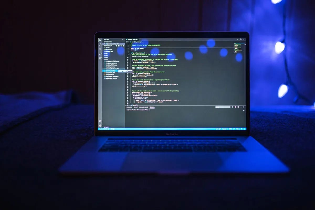 A laptop screen showing code in a dark, blue-lit workspace A laptop screen showing code in a dark, blue-lit workspace