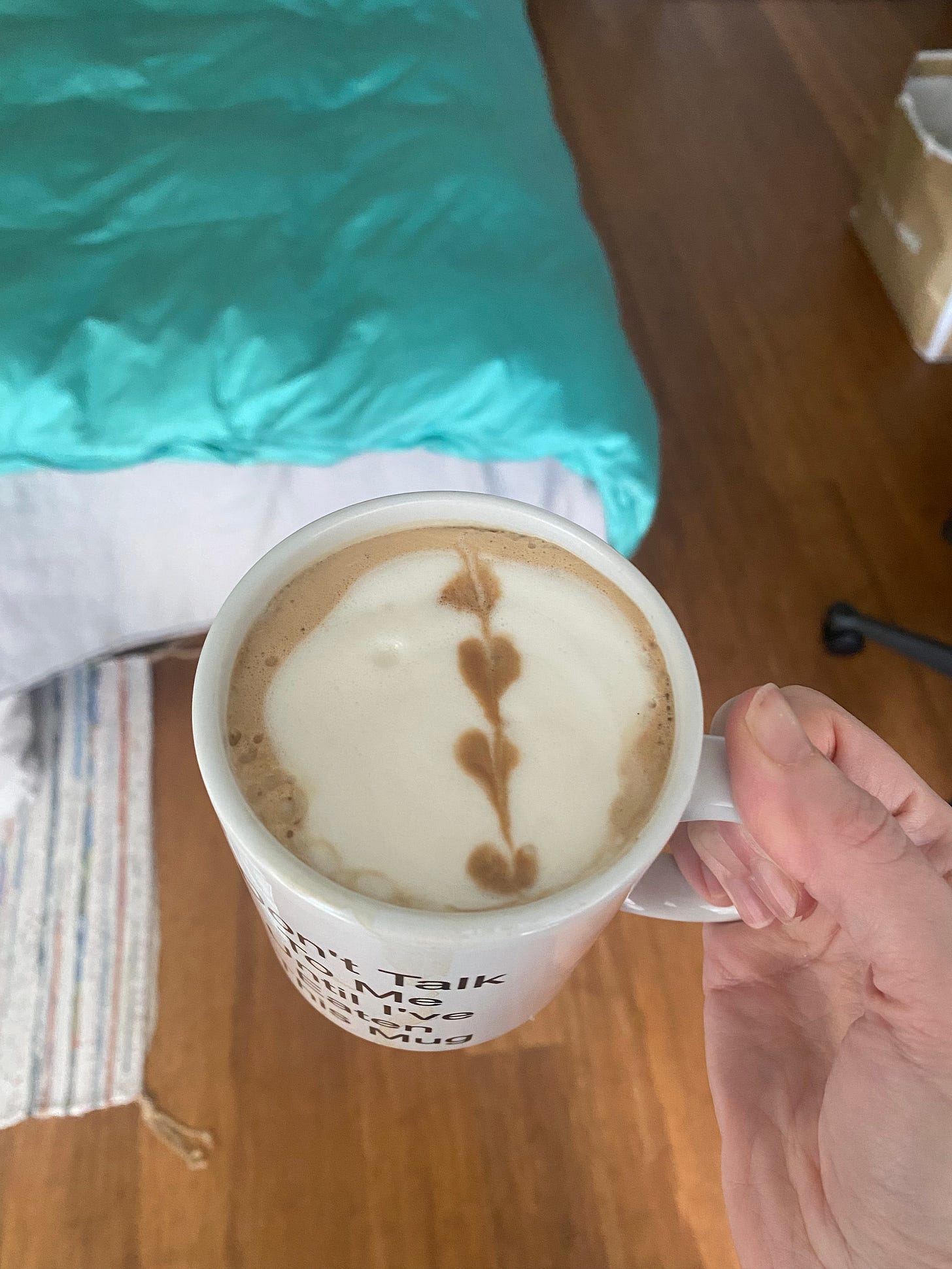 A white mug with a latte in it, a string of hearts (or heart-shaped leaves) drawn in the foam on top.