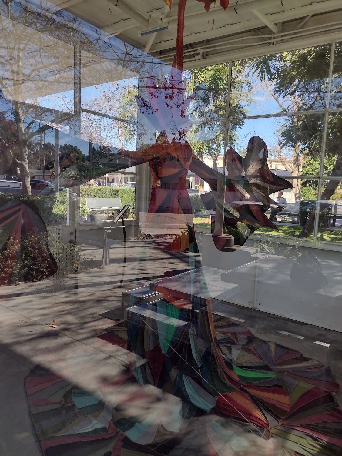 View through a sunlit window of a room sized kaleidoscopic robe with full sleeves and skirt and a flame ruff