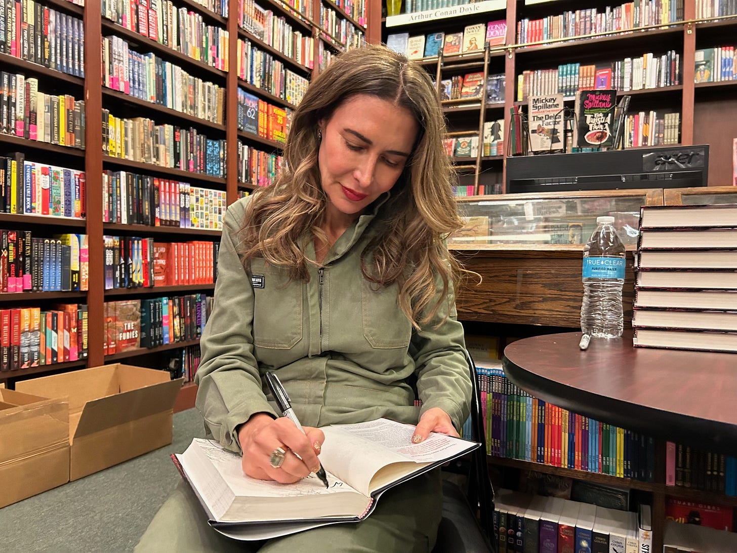 Image shows Abbott Kahler, seated, signing books at The Mysterious Bookshop