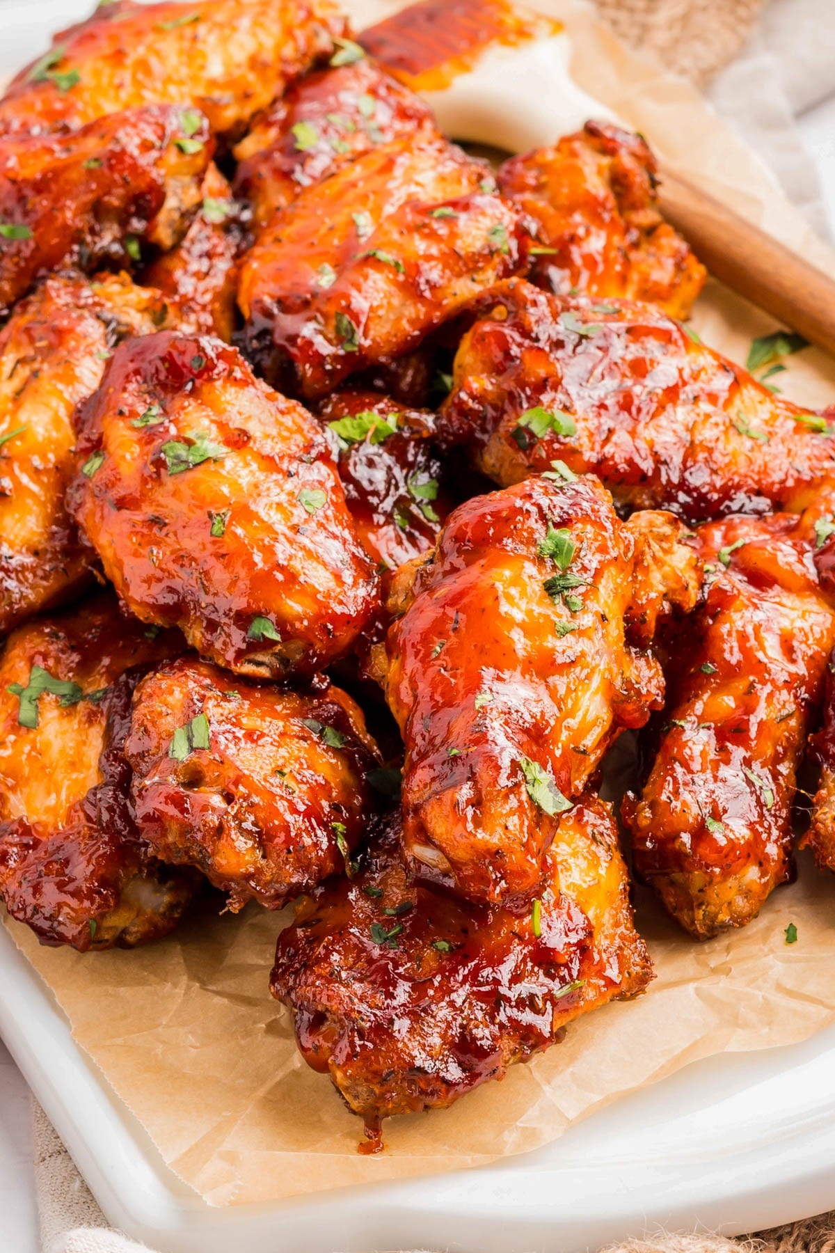 A tray of glazed chicken wings garnished with chopped herbs, placed on parchment paper, with a basting brush in the background. A tray of glazed chicken wings garnished with chopped herbs, placed on parchment paper, with a basting brush in the background.
