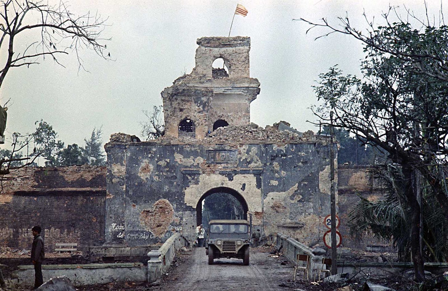 February 1968, Hue: The Republic of Vietnam flag flies over the old citadel as a jeep crosses a moat bridge amidst the Tet Offensive's intense fighting.
